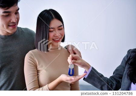 A young couple receives keys from a professional during a property handover. 131204786