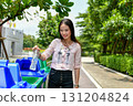 A young woman happily recycling a plastic bottle in an eco-friendly environment, promoting sustainability. 131204824
