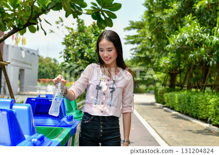 A young woman happily recycling a plastic bottle in an eco-friendly environment, promoting sustainability. 131204824