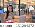 Young girl proudly holds cash near a laptop, representing financial success and ambition in the modern world. 131204872