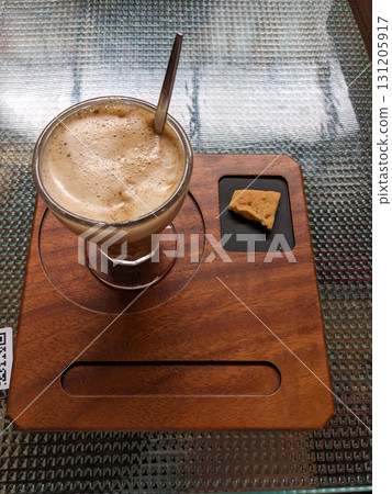A glass of foamy coffee is served with a cookie on a wooden tray, ready for a moment of relaxation. 131205917