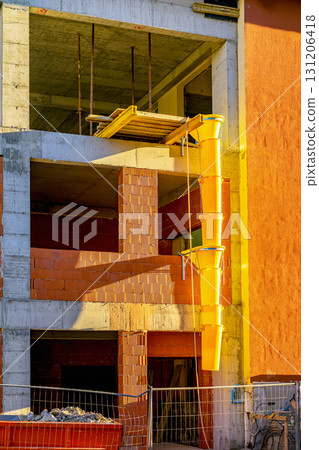 Bright yellow construction chute attached to unfinished building with exposed red bricks, scaffolding. Concept of construction work, debris disposal and building site 131206418