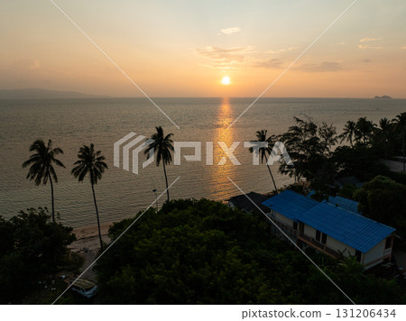 The calm sea glows under a golden sunset with palms standing tall along the coastline. Ko Pha Ngan, Thailand. The calm sea glows under a golden sunset with palms standing tall along the coastline. Ko Pha Ngan, Thailand. 131206434
