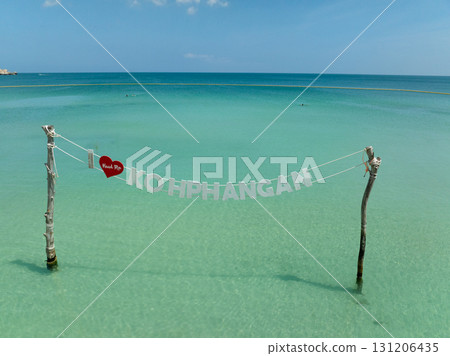 Koh Phangan sign above turquoise waters, supported by wooden poles, under a clear blue sky. Ko Pha Ngan, Thailand. 131206435