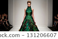 A female model walks confidently on the runway, wearing an elaborate dress crafted from shimmering green beetle wings. The creative design captures the attention of the audience seated nearby. 131206607