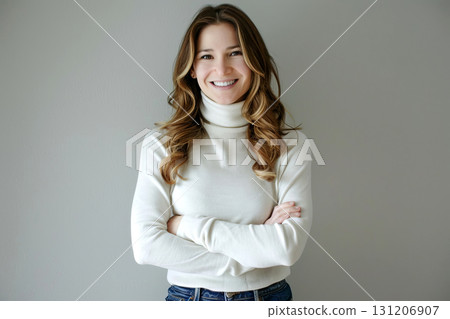 Woman with long hair smiles confidently while wearing a white turtleneck sweater, arms crossed, in a bright indoor setting 131206907