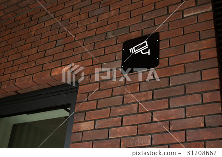 Security camera sign mounted on brick wall, indicating surveillance, commonly seen in commercial and residential properties to enhance safety and monitor activity 131208662