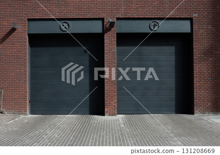 Modern garage doors with sleek black panels and symbolic icons, set against brick wall. The clean lines and geometric design create a minimalist and industrial aesthetic 131208669