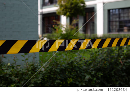 Close up of yellow and black caution tape, symbolizing hazard zone. The blurred background of the building adds depth, reinforcing the idea of secure or restricted area Close up of yellow and black caution tape, symbolizing hazard zone. The blurred background of the building adds depth, reinforcing the idea of secure or restricted area 131208684