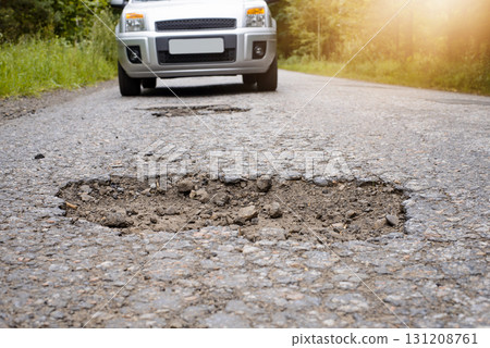 SIlver car driving on highway and approaching big deep pothole. Concept of terrible road, road needs repairing 131208761