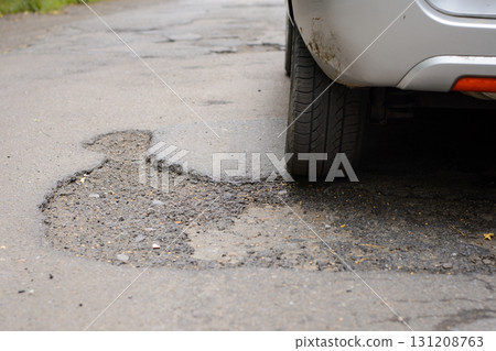Rear wheel of a car moving through many potholes on bad road 131208763