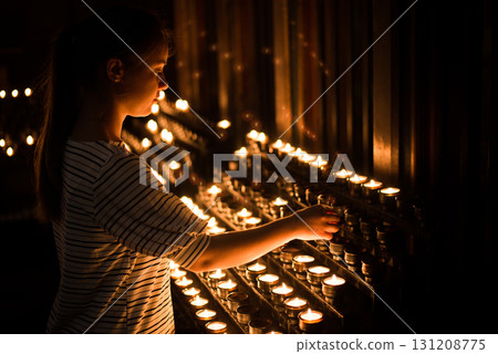 Religious woman putting burnng candle between many other church candles, praying for someone Religious woman putting burnng candle between many other church candles, praying for someone 131208775