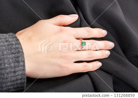 Beautiful female hand with gold ring with diamonds and emerald on gray background Beautiful female hand with gold ring with diamonds and emerald on gray background 131208850