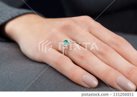 Beautiful female hand with gold ring with diamonds and emerald on gray background Beautiful female hand with gold ring with diamonds and emerald on gray background 131208851