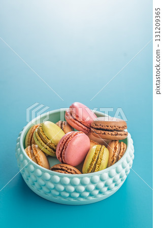 Different flavors of macarons. Colourful macaroons in bowl on blue background. Different flavors of macarons. Colourful macaroons in bowl on blue background. 131209365