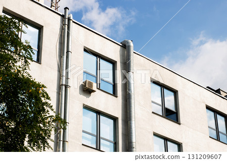 A tall building featuring numerous windows along with a chimney on its side 131209607