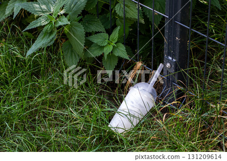 A white cup with a straw is in the grass by a fence post 131209614
