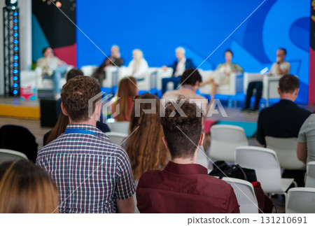 Panel discussion at a conference with diverse speakers and attentive audience on a colorful stage Panel discussion at a conference with diverse speakers and attentive audience on a colorful stage 131210691