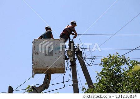 Electricians are diligently working on overhead power lines high above the ground, ensuring Electricians are diligently working on overhead power lines high above the ground, ensuring 131210814