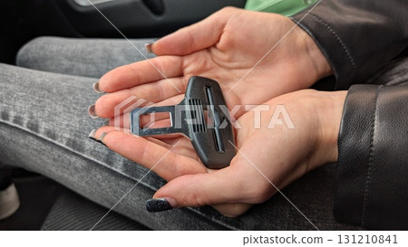 A hand is securely holding a car seat belt buckle inside a vehicle for safety during travel 131210841