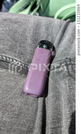 A stylish purple vaping device rests on trendy denim jeans, showcasing its modern aesthetic 131210864