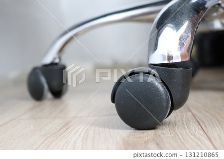 A closeup view of rolling office chair casters positioned on a wooden floor surface 131210865