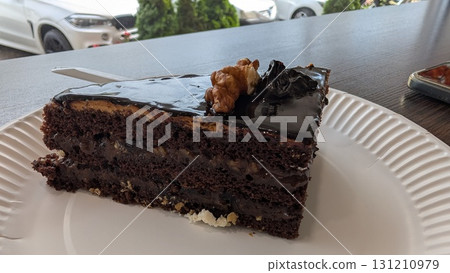 Indulgent Slice of Decadent Chocolate Cake Decorated with Nuts and Creamy Frosting 131210979