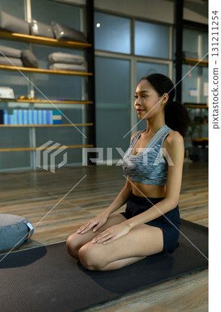Young woman sitting in yoga pose on mat in fitness studio. Mindfulness concept Young woman sitting in yoga pose on mat in fitness studio. Mindfulness concept 131211254