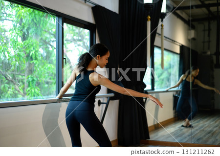 Young woman practicing ballet at barre in studio, focusing on graceful arm movements Young woman practicing ballet at barre in studio, focusing on graceful arm movements 131211262
