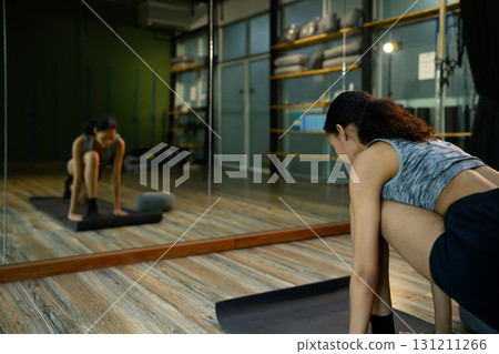 Young woman practicing yoga pose on mat in fitness studio with mirror reflection 131211266