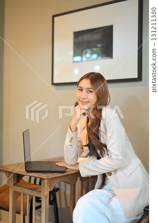 Young woman smiling at the camera while working with a laptop in a modern cafe 131211380