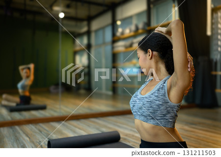 Young woman stretching arms behind head on yoga mat in modern fitness studio Young woman stretching arms behind head on yoga mat in modern fitness studio 131211503