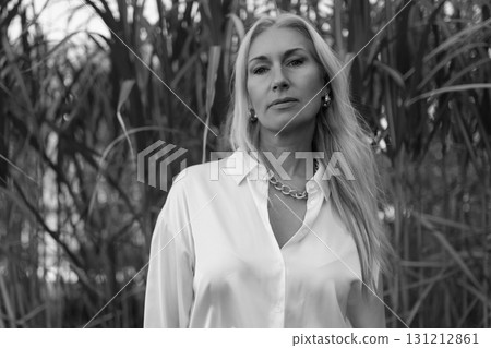 Woman in white shirt stands confidently among tall grass during golden hour Woman in white shirt stands confidently among tall grass during golden hour 131212861