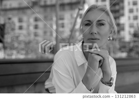 Woman sitting outdoors with a thoughtful expression in an urban park during the daytime 131212863