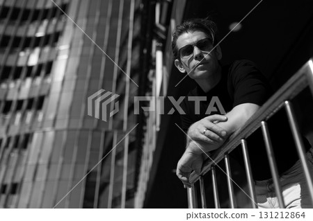 Man in sunglasses leans on railing in urban setting during bright daylight 131212864