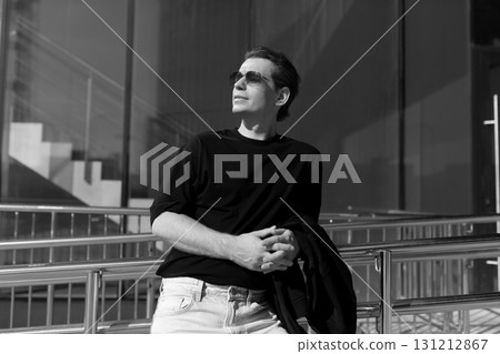Man in sunglasses stands confidently outside a modern building on a sunny day with a relaxed pose Man in sunglasses stands confidently outside a modern building on a sunny day with a relaxed pose 131212867