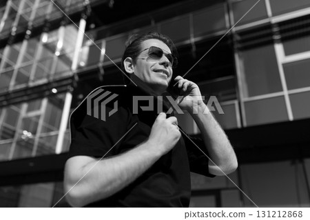 Man in sunglasses making a phone call outside modern building on a sunny day Man in sunglasses making a phone call outside modern building on a sunny day 131212868