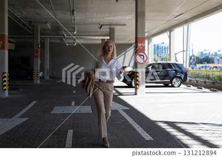 Woman walking confidently in a parking garage while checking her phone during daylight hours 131212894