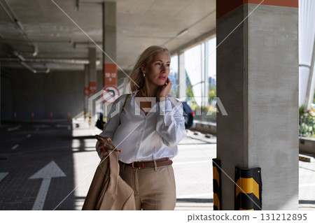 Woman in elegant attire stands in parking garage during daylight, looking thoughtfully while 131212895