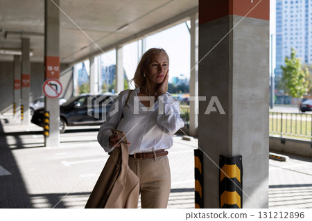 Woman in elegant attire with coat in a parking structure during daylight hours 131212896