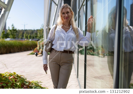 Stylish woman poses confidently near modern building on a sunny day, showcasing a chic outfit and a Stylish woman poses confidently near modern building on a sunny day, showcasing a chic outfit and a 131212902