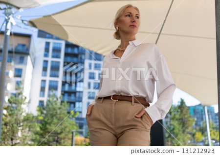 Model posing confidently in outdoor urban setting with modern architecture and bright sunlight 131212923