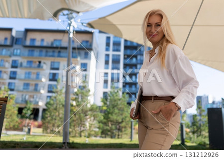 Businesswoman smiles outdoors at a modern apartment complex during daytime in a relaxed setting 131212926