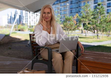 Professional woman working on laptop outside in modern urban park setting during sunny day Professional woman working on laptop outside in modern urban park setting during sunny day 131212936