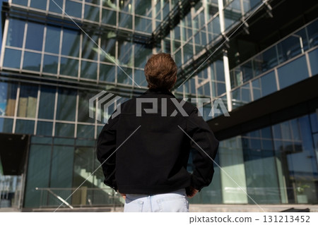 Man admires modern architecture of glass building under clear blue sky during daylight Man admires modern architecture of glass building under clear blue sky during daylight 131213452