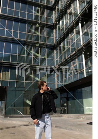 Young man talking on the phone in front of modern glass buildings during a sunny day 131213460