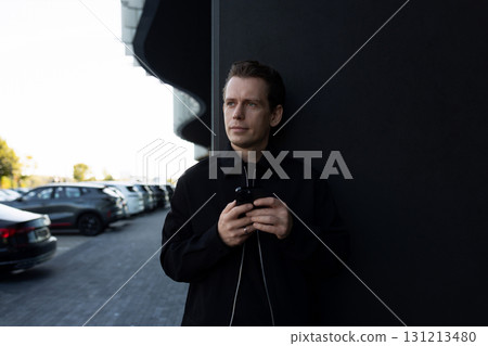 Man standing with phone by modern building during daylight in urban setting 131213480