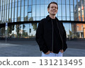 Young man smiling confidently in front of a modern building during the daytime 131213495