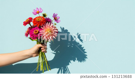 A hand holds a beautiful, elegant bouquet of fresh flowers against a bright, light blue background 131213688
