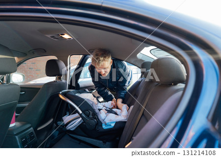 Father putting baby in safety car seat happy family vacation road trip lifestyle child care transportation rear-facing. Caring parent secures baby by fastening with seat belt. Selective focus. Father putting baby in safety car seat happy family vacation road trip lifestyle child care transportation rear-facing. Caring parent secures baby by fastening with seat belt. Selective focus. 131214108